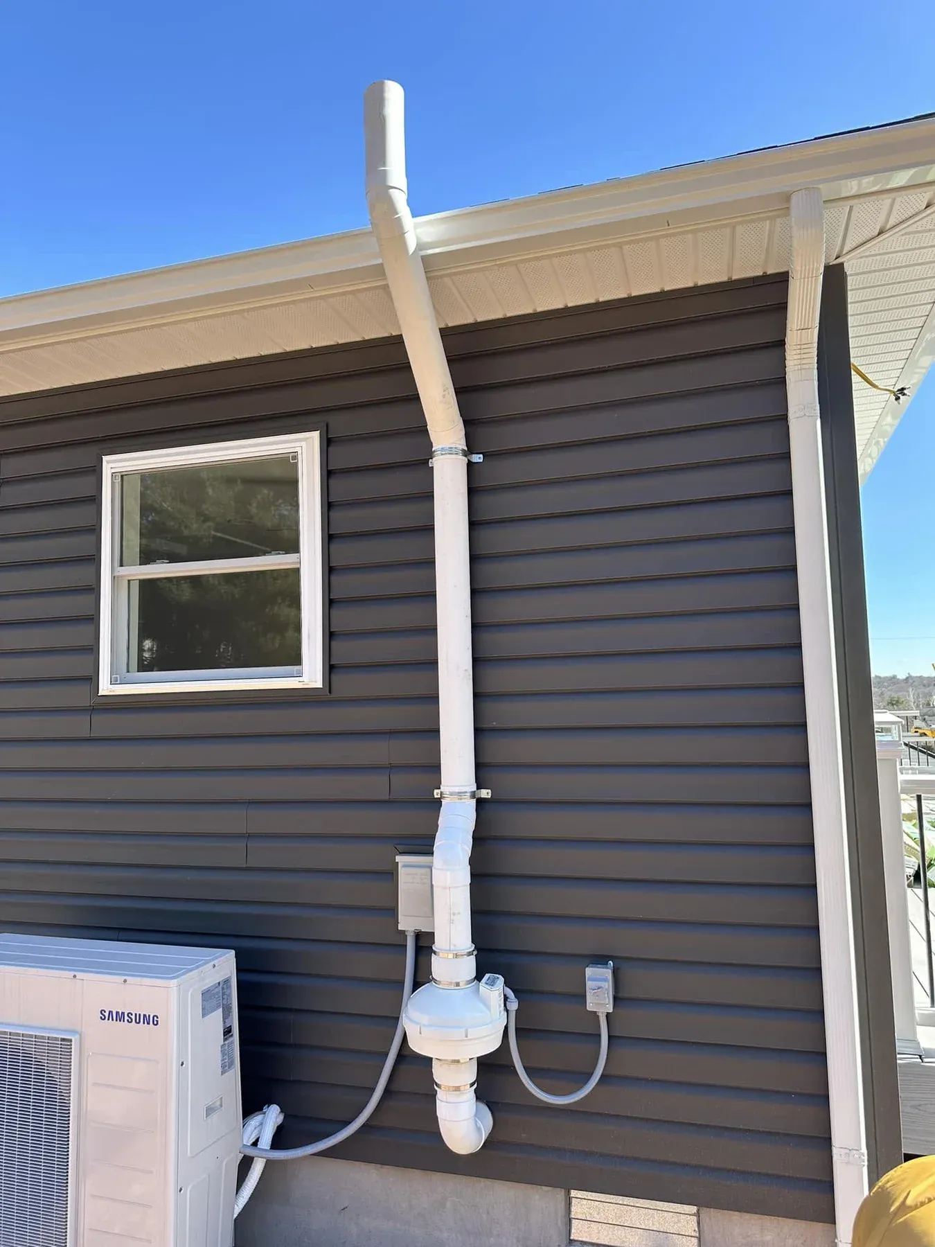 Exterior radon mitigation fan and vent pipe installed on dark siding