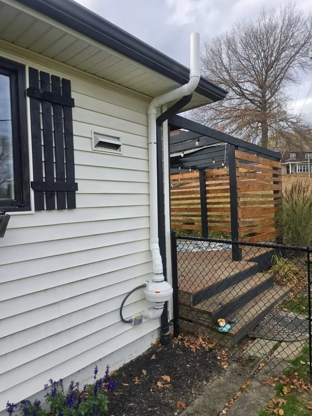 Radon mitigation fan and vent pipe installed against light-colored siding